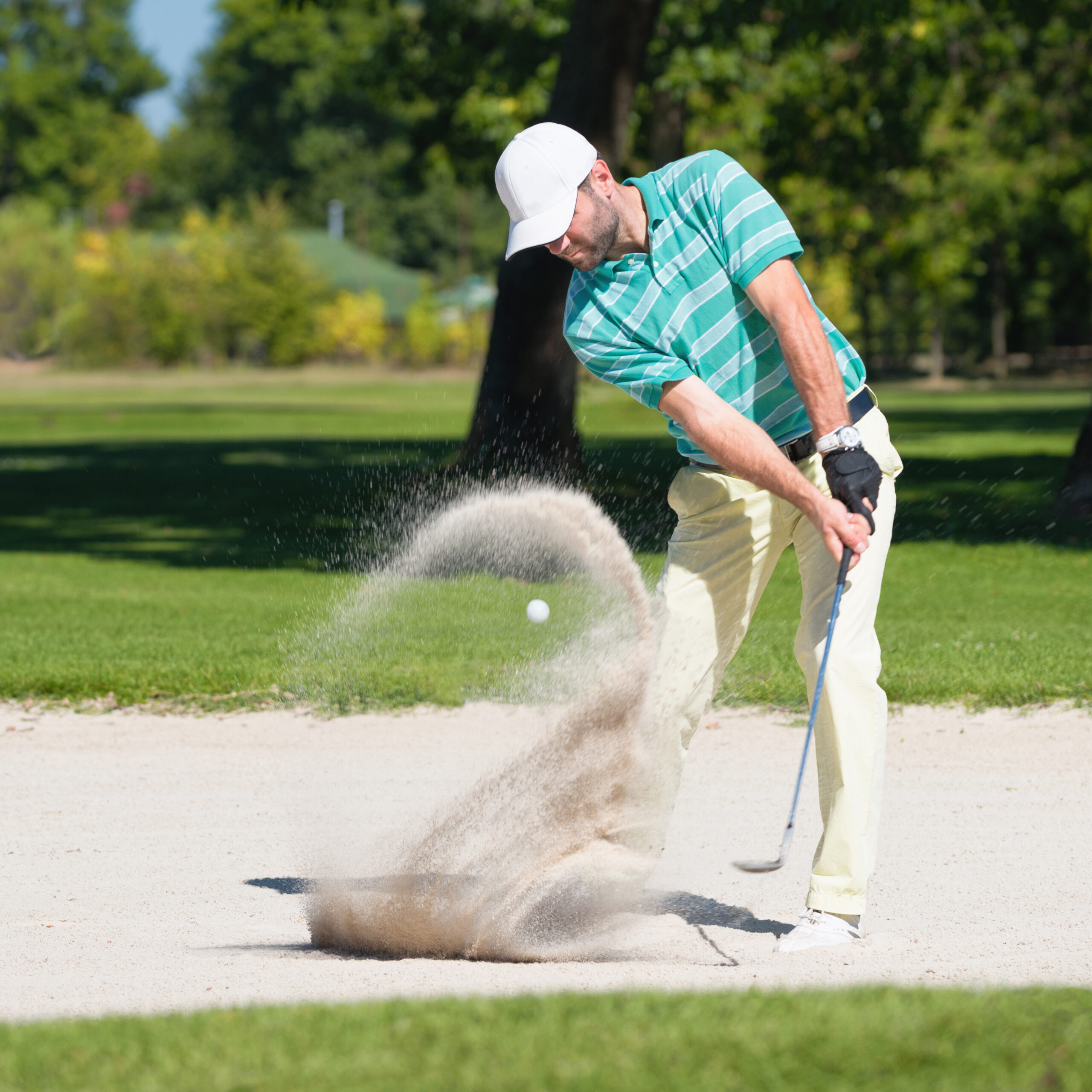 Golfer hits the ball out of sand trap. Focus on golfer, ball and sand wave in motion blur.